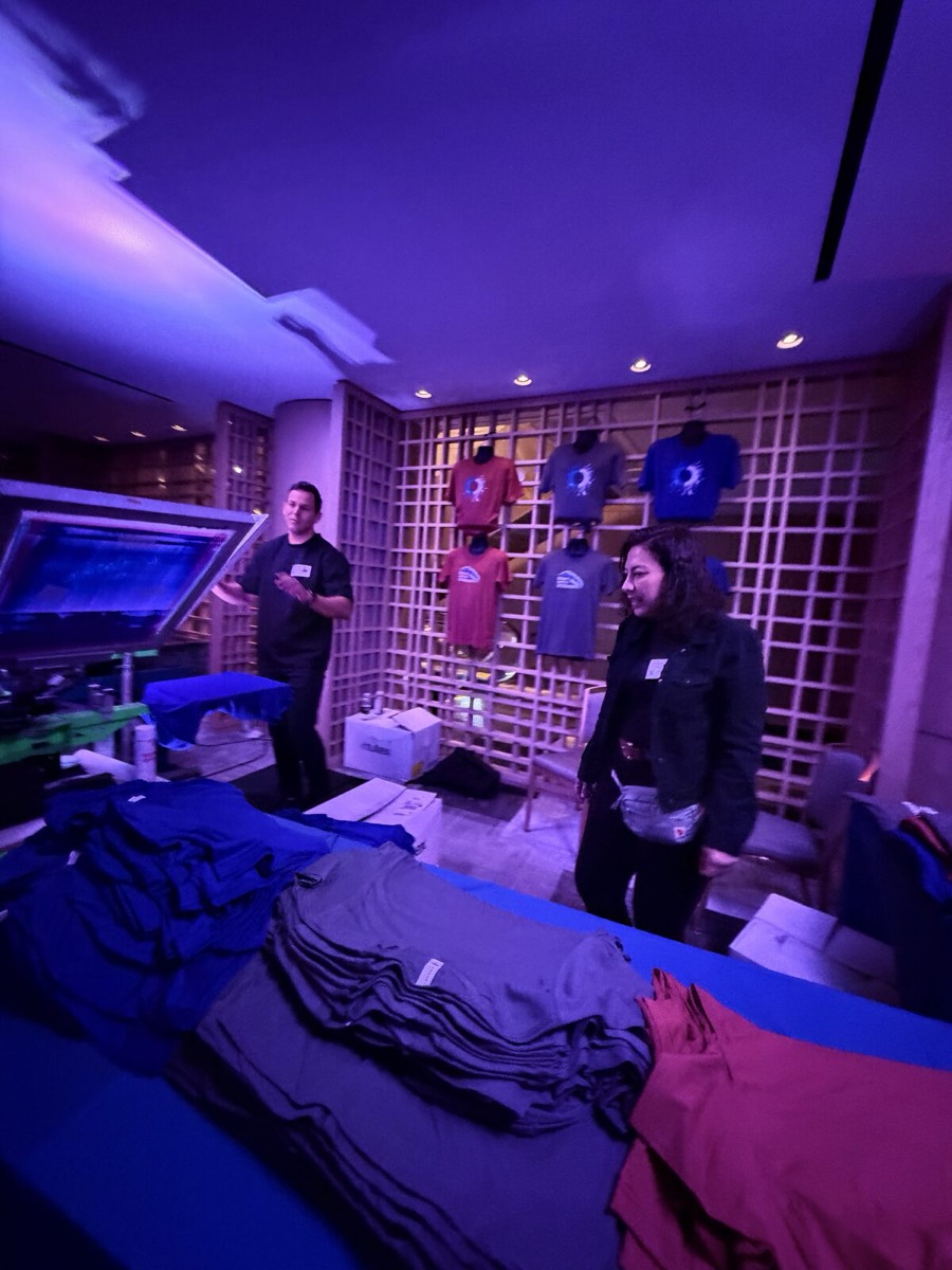 Apparel display wall and folded garment table under violet uplighting in a hotel suite activation