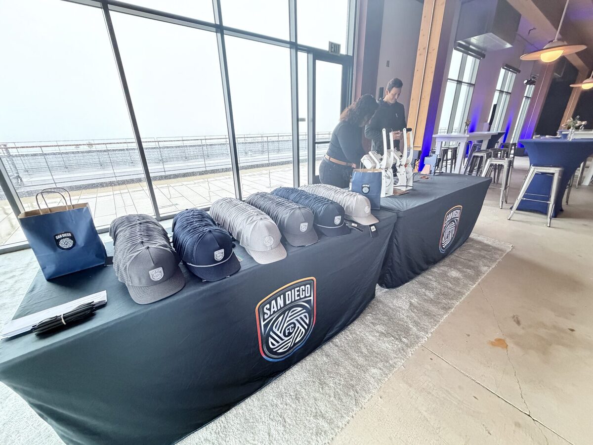 Rows of curated caps arranged on a black-draped personalization table at a rooftop club event